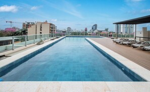 A rooftop swimming pool with a city view, lounge chairs, and a wooden deck.