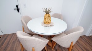 Ein runder Tisch mit einer Ananas als Mittelstück, umgeben von vier Stühlen mit Holzbeinen und Stoffsitzen.