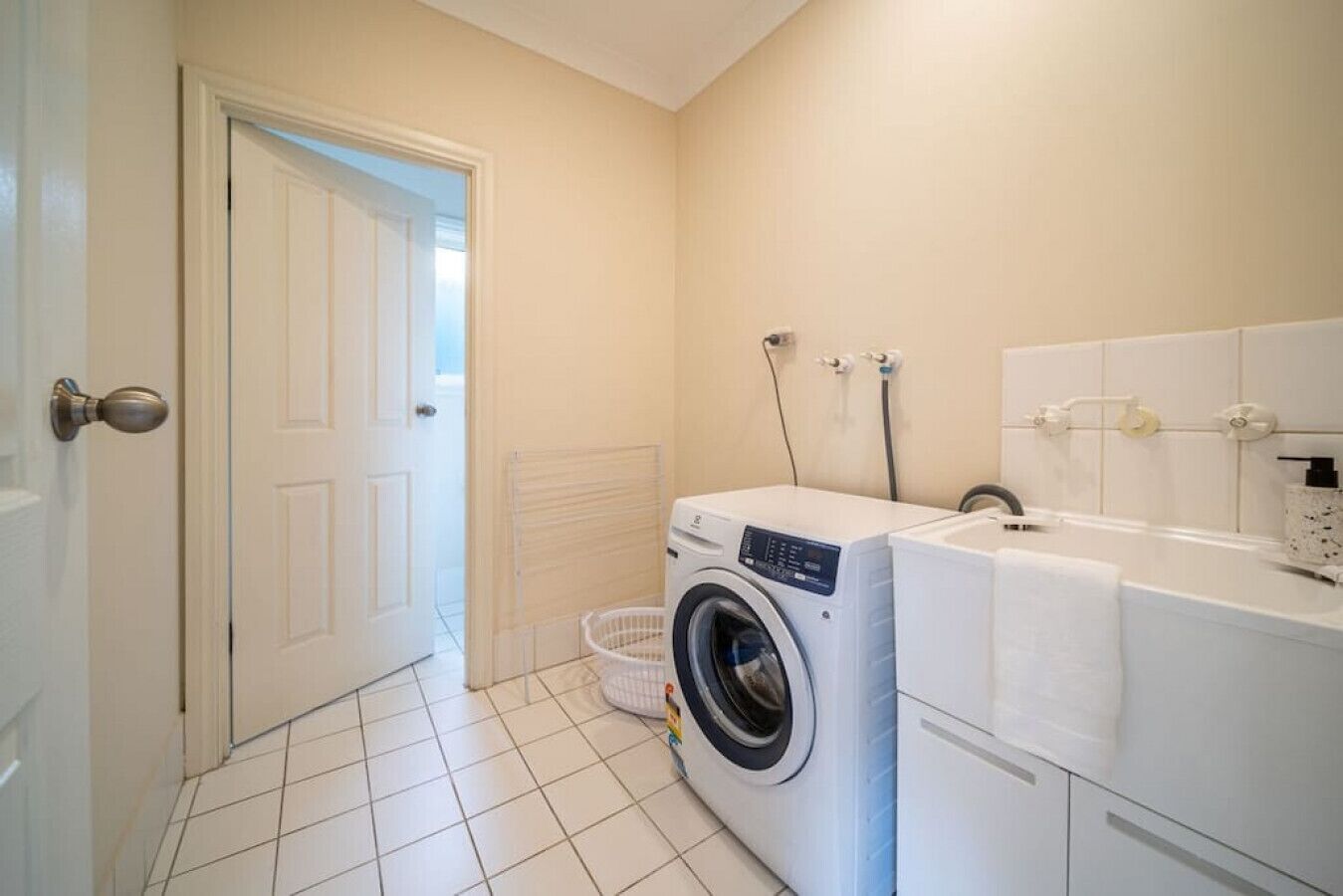 Une buanderie équipée d’un lave-linge et d’un sèche-linge à chargement frontal, d’un étendoir et d’un sol carrelé de couleur blanche.
