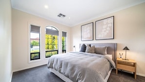 A bedroom with a large bed, two bedside tables, and a view of greenery through the windows.