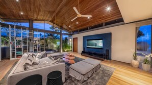 A modern living room with a large TV, comfortable seating, and a view of the outdoors. - Villa Tievoli (Takua Thung)