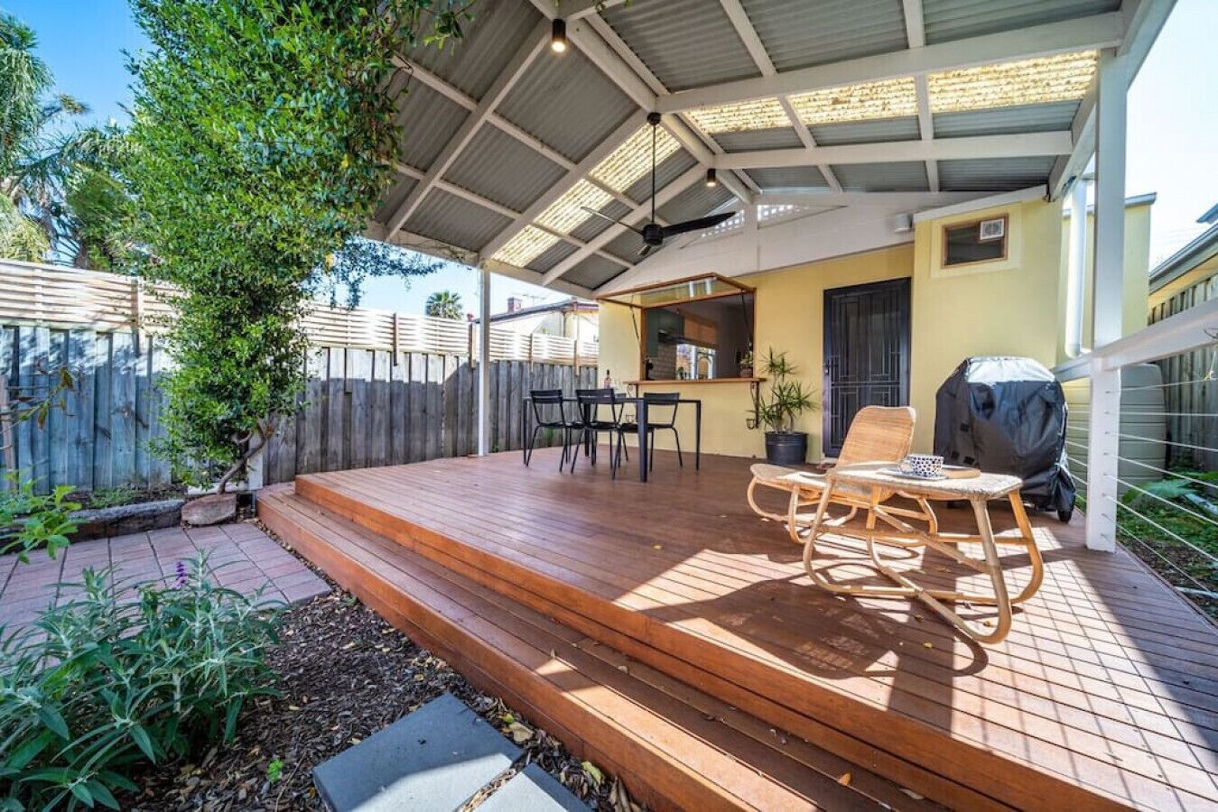 Eine überdachte Terrasse mit Holzdeck, Gartenmöbeln und einem Grill.