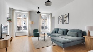 A modern living room with a grey sectional sofa, a small round table, and a TV on a wooden stand.