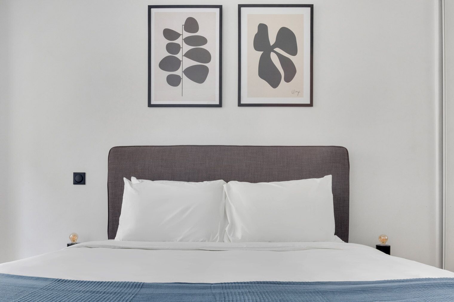 Ein Schlafzimmer mit einem Bett, zwei gerahmten Kunstwerken an der Wand und einem Nachttisch mit einer Lampe.