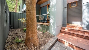 A modern house with a large tree in the backyard, a patio with outdoor furniture, and a staircase leading to the entrance. - Juniper on Rundle - A Leafy City-fringe Escape (Kent Town)