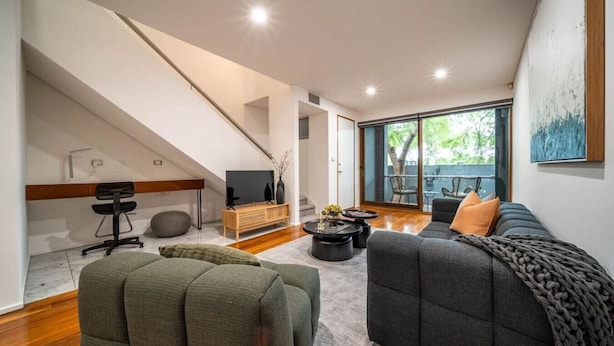 A modern living room with a staircase, a sofa, a coffee table, and a TV. - Juniper on Rundle - A Leafy City-fringe Escape (Kent Town)