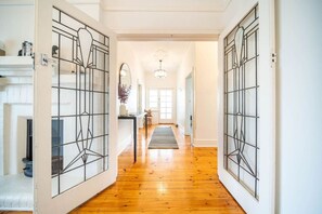 A hallway with wooden flooring, white walls, and a door with a geometric glass design. - Redgum on Rugless—Coastal Charm near Glenelg Beach (Glenelg East)