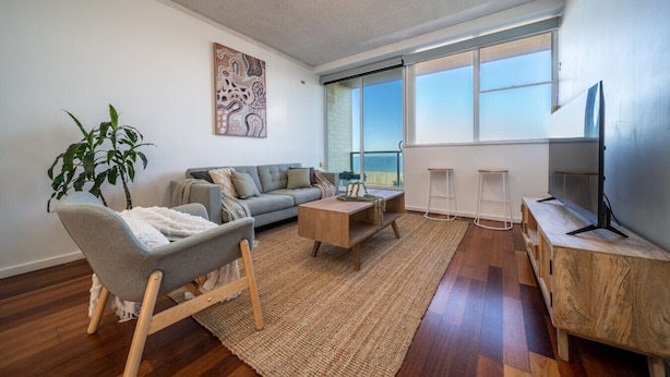 A modern living room with a sofa, coffee table, TV stand, and a large window with a view.