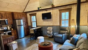 Ein gemütliches Blockhaus-Interieur mit Holzwänden, einer Küche mit modernen Geräten, einer komfortablen Sitzecke und einem großen Fenster, das für natürliches Licht sorgt.