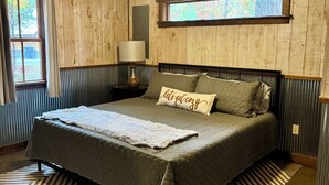 Ein Schlafzimmer mit einem großen Bett, Holzwänden, einem Fenster und einer Deckenleuchte.