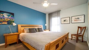 A bedroom with a wooden bed, a nightstand, a desk lamp, a chair, and artwork on the walls. - Get Comfy on Frew - CBD Stay near Parklands & Dining (Adelaide)