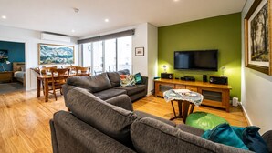 A living room with a sofa, a dining table, and a TV. - Get Comfy on Frew - CBD Stay near Parklands & Dining (Adelaide)