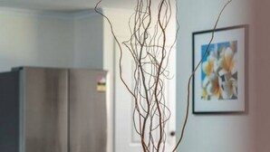 A dining area with a wooden table, chairs, a vase with branches, a refrigerator, and a framed picture on the wall. - Escape to Adelaide Hills—Spacious Country Stay (Nairne)