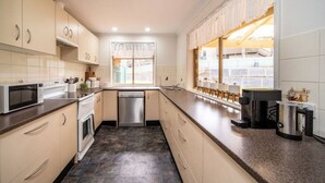 A modern kitchen with beige cabinets, a stainless steel dishwasher, a microwave, and a coffee maker. - Escape to Adelaide Hills—Spacious Country Stay (Nairne)