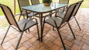 An outdoor patio with a table and chairs, a potted plant, and a view of a tennis court. - Escape to Adelaide Hills—Spacious Country Stay (Nairne)