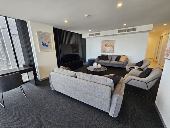A modern living room with a grey sofa, a black entertainment unit, and a flat-screen TV.