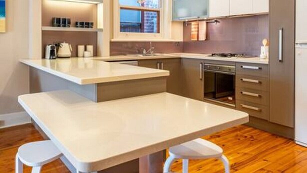 A modern kitchen with a central island, white cabinetry, and a wooden floor. - The Fourth @ Sussex House—Beach Ease off Jetty Rd (Glenelg)