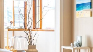 A modern living room with a round coffee table, two white vases with branches, a patterned rug, and a view of the outdoors through large windows. - The Fourth @ Sussex House—Beach Ease off Jetty Rd (Glenelg)