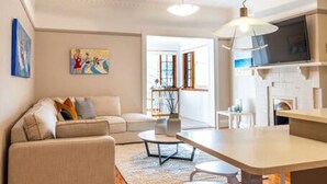 A modern living room with a sofa, a dining table with chairs, and a kitchen area with a TV. - The Fourth @ Sussex House—Beach Ease off Jetty Rd (Glenelg)
