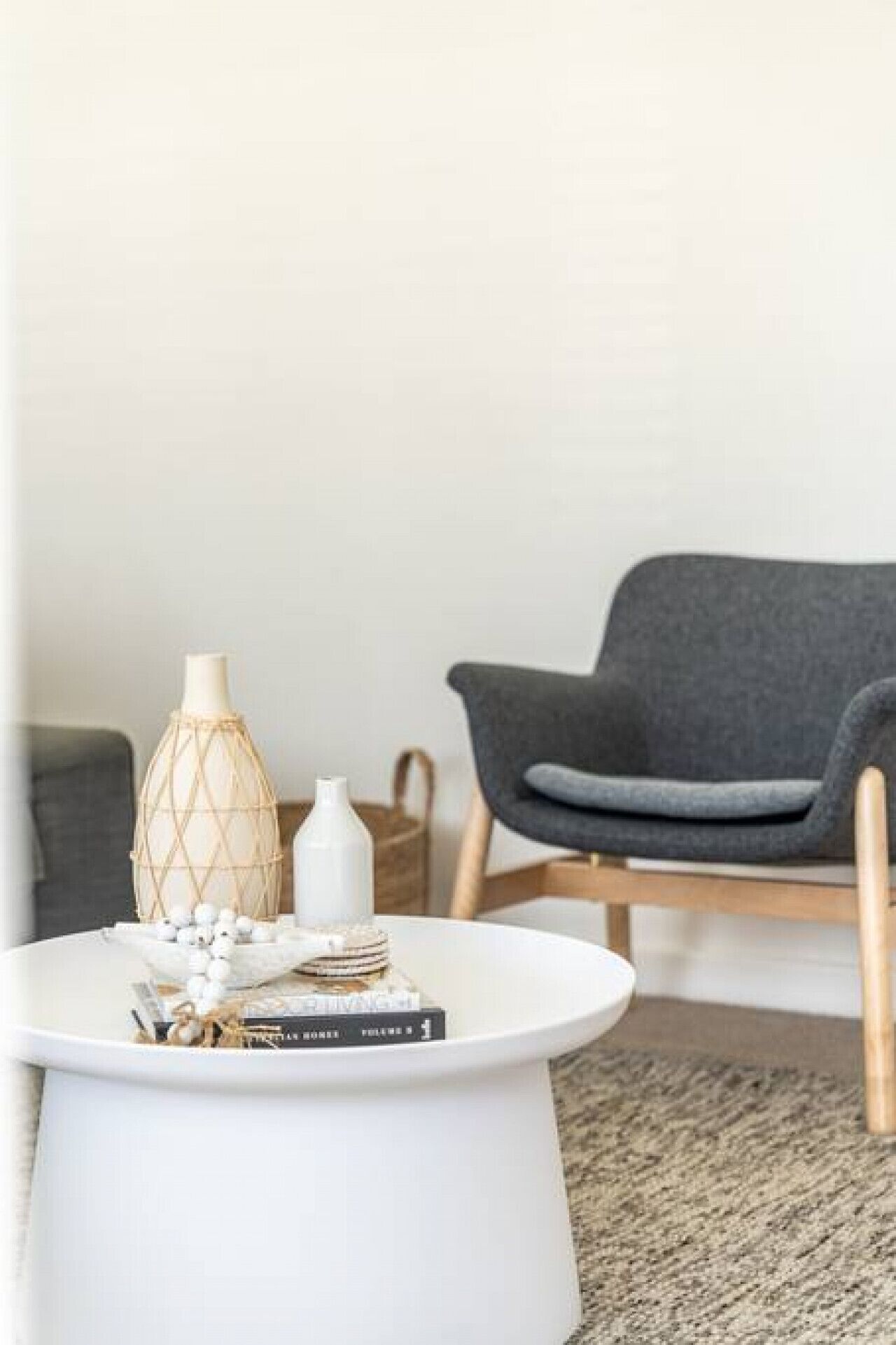 Un salón moderno con una mesa de centro blanca, un sillón gris y una lámpara de fibras naturales.