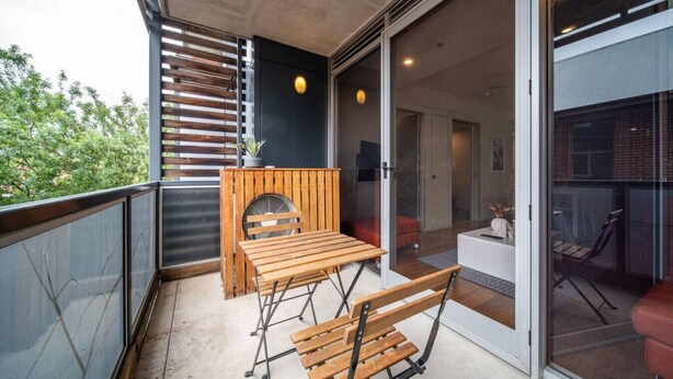 A balcony with a wooden table and chairs, a potted plant, and a sliding glass door leading to an interior space. - Huttside - Comfortable CBD Stay near Parklands (Adelaide)