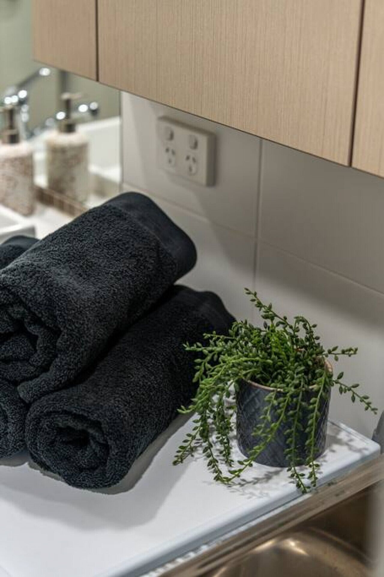 Un baño con encimera blanca, una toalla enrollada y una pequeña planta en maceta.