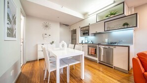 A modern kitchen with white cabinetry, stainless steel appliances, and a dining area with a white table and chairs. - Huttside - Comfortable CBD Stay near Parklands (Adelaide)