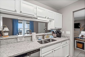 A modern kitchen with white cabinets, a granite countertop, a double sink, and a coffee maker.