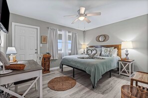 A bedroom with a bed, bedside tables, a desk, a ceiling fan, and a window with curtains.