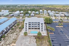 A multi-story hotel with a swimming pool, parking lot, and surrounding greenery.