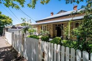 A stone house with a white picket fence, a front porch, and a brick pathway.