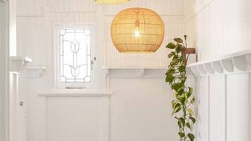 A hallway with wooden flooring, white walls, a wooden bench, and two hanging wicker lamps.
