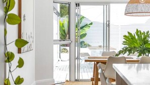 Uma sala de jantar moderna com uma mesa e cadeiras de madeira, um tapete tecido e vista para o exterior através de grandes portas de vidro.