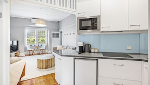 Una cocina moderna con armarios blancos, microondas, cafetera y refrigerador pequeño.