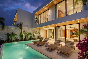 A modern two-story house with a swimming pool, outdoor seating, and a well-lit interior. - Private Infinity Pool | Ocean Views | Beach Access (Uluwatu)