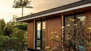 A modern building with large windows, wooden paneling, and a well-maintained garden with various plants and a palm tree.