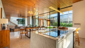 A modern kitchen with a marble island, wooden ceiling, and large windows.