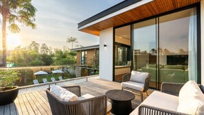 A modern outdoor deck with wicker furniture, a round table, and a glass-enclosed area with green sofas.