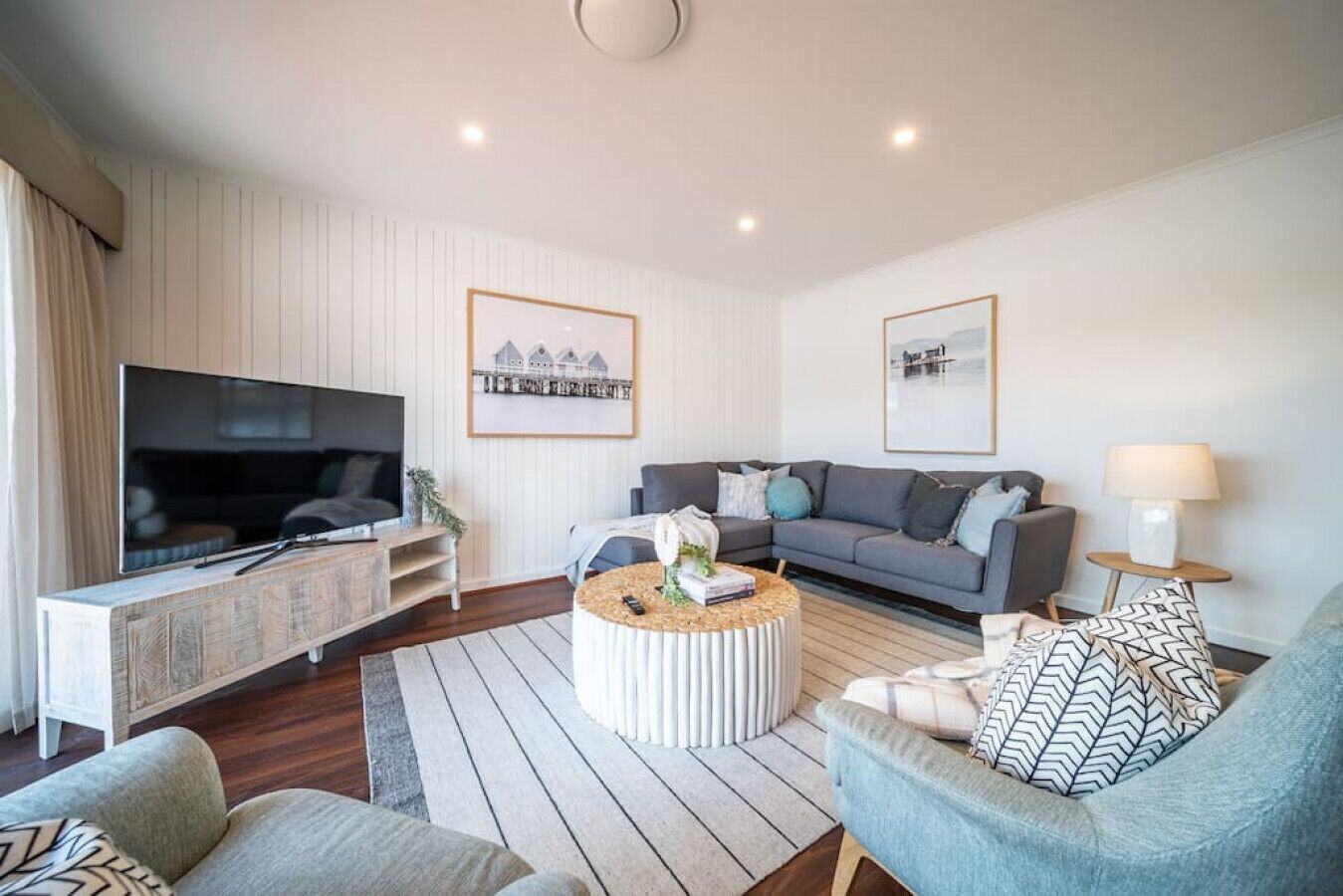 Una sala de estar moderna con televisor de pantalla plana, sofá gris, mesa redonda de centro y un sillón estampado.