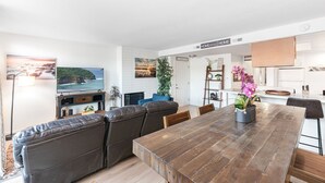 Uma sala de estar moderna com uma mesa de jantar de madeira, sofás de couro, uma televisão e uma área de cozinha com bancada de madeira.
