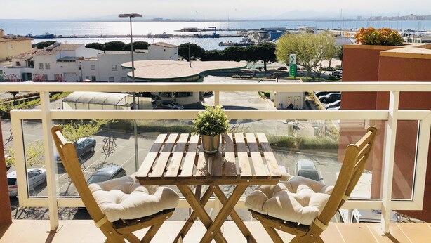 Ein Balkon mit Tisch und Stühlen mit Blick auf eine Marina, in der Boote und Gebäude liegen.