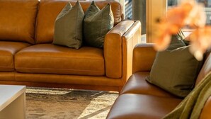 A modern living room with a brown leather sofa, a glass balustrade, and a view of the cityscape. - The Views Penthouse - Cityscape & Parkland Scenery (Adelaide)