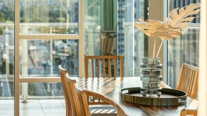 A dining area with a large window, wooden chairs, a glass table, and a decorative glass sculpture. - The Views Penthouse - Cityscape & Parkland Scenery (Adelaide)