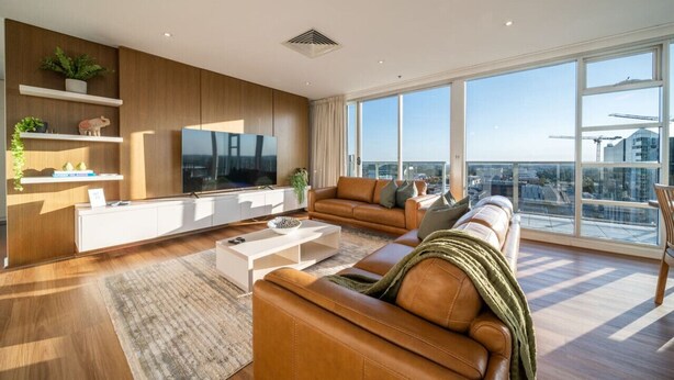 A modern living room with a large TV, leather sofas, a coffee table, and a view of the city through large windows. - The Views Penthouse - Cityscape & Parkland Scenery (Adelaide)