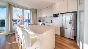 A modern kitchen with white cabinetry, a stainless steel refrigerator, and a large island with bar stools. - The Views Penthouse - Cityscape & Parkland Scenery (Adelaide)