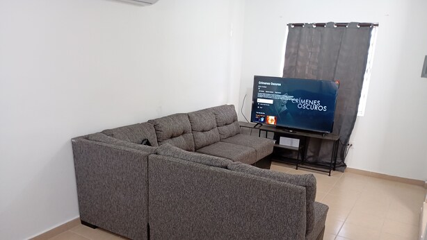 A grey sectional sofa in a living room with a flat-screen TV on a stand. - Casa 2 recámaras zona aeropuerto clima total (Pesquería)
