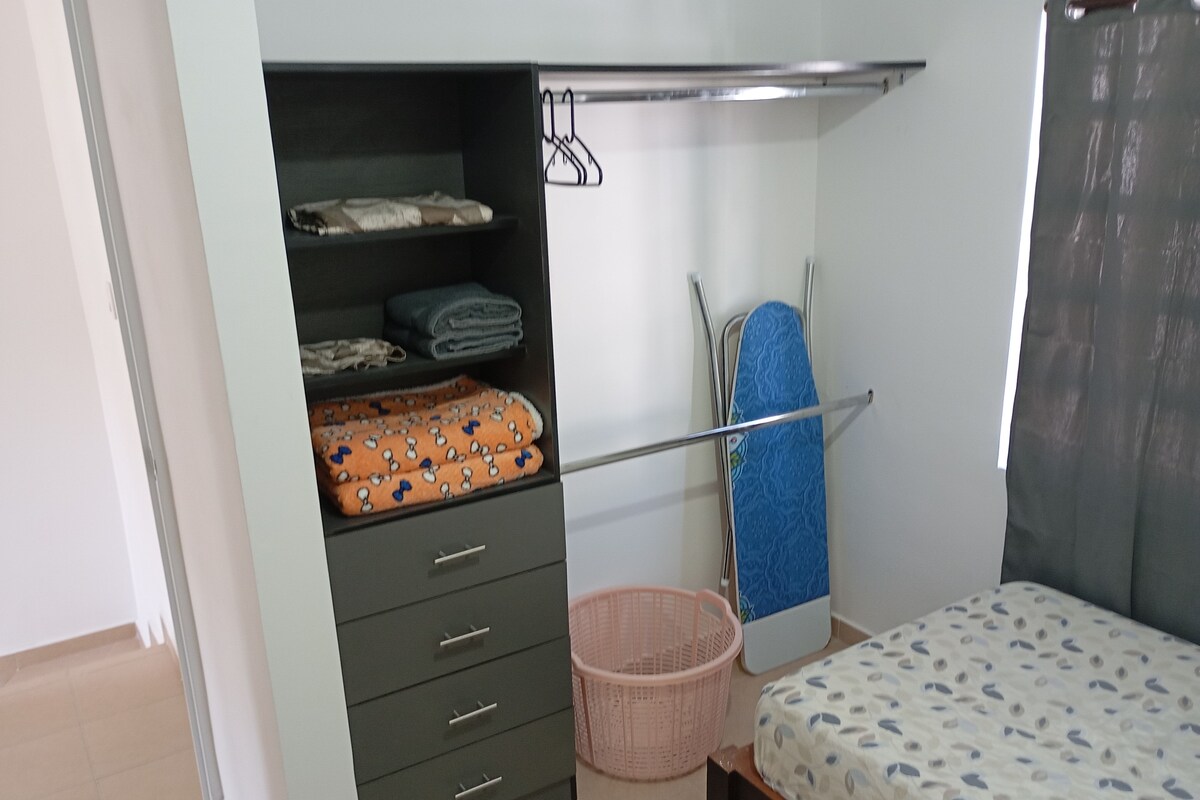 A bedroom with a bed, a wardrobe, a hanging rack, and a laundry basket.