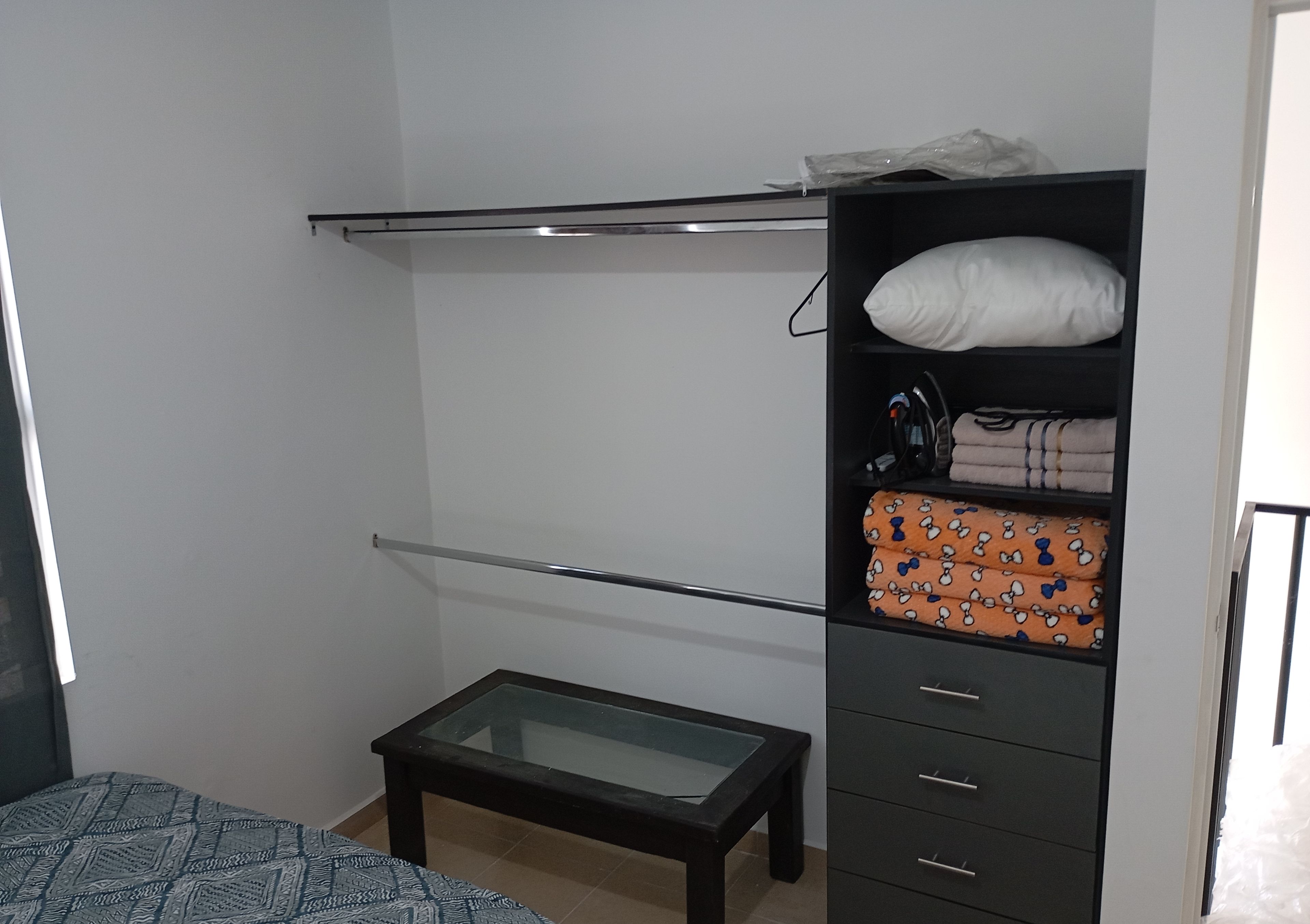 Un dormitorio con literas, una mesita pequeña, un armario con cajones y una cama con una colcha estampada.