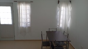 A room with a dining table, chairs, a window with curtains, a door, and a ceiling light. - Casa 2 recámaras zona aeropuerto clima total (Pesquería)