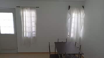 Ett rum med ett matbord, stolar, ett fönster med gardiner, en dörr och en taklampa.